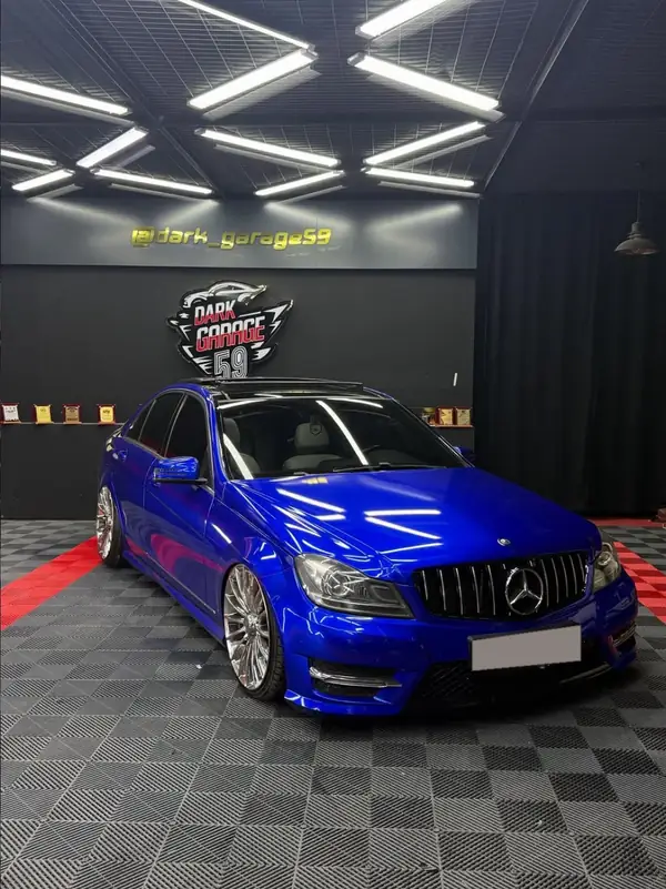 Dark Garage 59 tabelasının önünde parlak mavi Mercedes C Serisi
